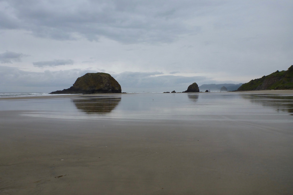 A sandy foreground, cloudy skies, and sea stacks in the distance